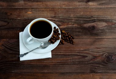 Bir fincan kahve koyu ahşap zemin üzerine kahve çekirdekleri ile.