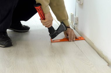 Yenileme bir apartman döşeme adam oda içinde döşeme laminant. Laminat kurulu odanın köşesinde bastırıp sıkıştırmak için metal bir çubuk ekler ve onu gömer.