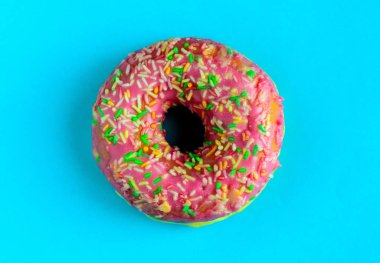 Mavi arka plan üzerinde pembe sırlı çörek. Şekerli tatlı.