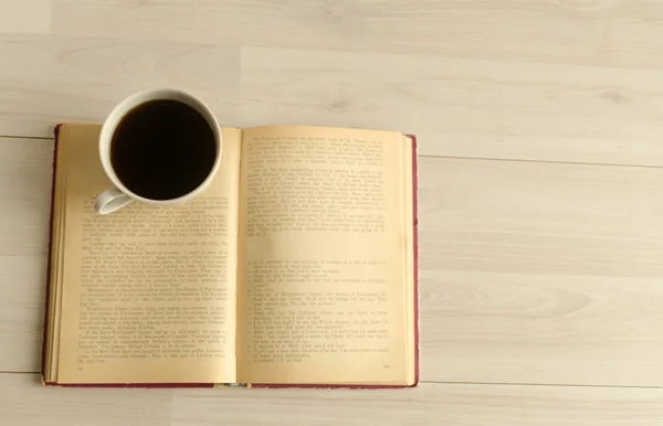 Een kopje koffie en een open boek op witte houten achtergrond. Bovenaanzicht, ruimte voor tekst. — Stockfoto