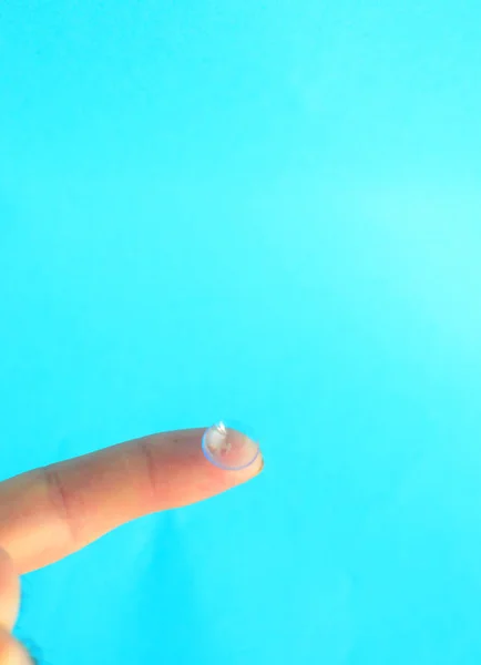 Lentille de contact sur le doigt sur fond bleu clair. . — Photo
