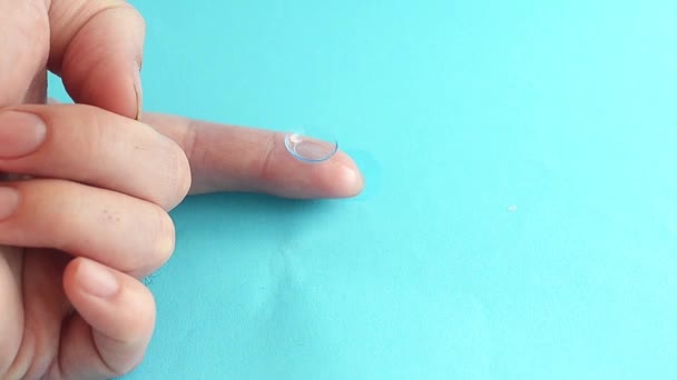 Een druppel van de universele oplossing druppels de contact lens liggend op de Mans vinger. Reinigen en wassen contactlenzen. Wijsvinger op blauwe achtergrond. — Stockvideo