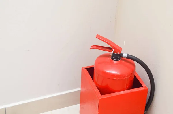 Red fire extinguisher in a metal container in the corner of a white wall.Safety.