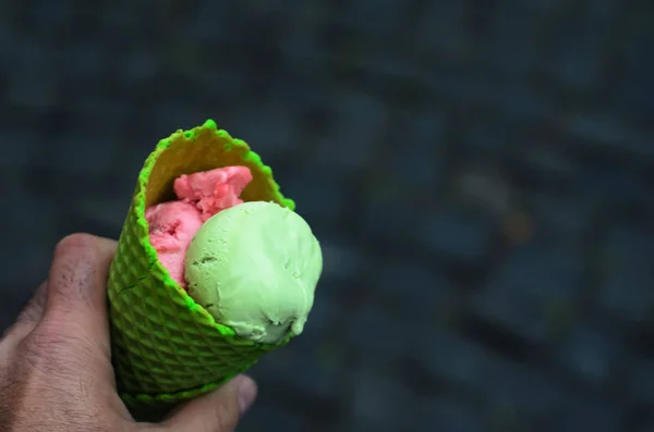 a man holding a green tube of strawberry and pistachio ice cream on a background of gray stone pavement.Close up,space for text.