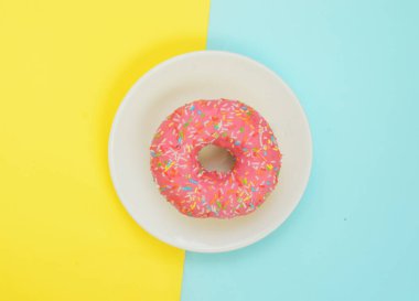 Üst manzara, beyaz tabakta pembe jöleli donut pastel sarısı turkuaz arka plan