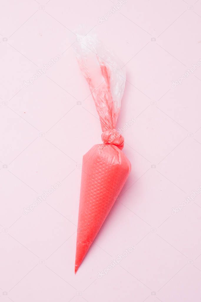 Close up of colored piping bag with red frosting inside over a pink background, top view