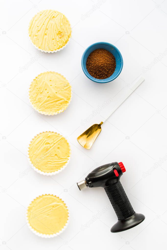 Rows of Creme catalana or creme brulee prepared to be caramelized, with a golden white spoon, a blowtorch and brown cane sugar.