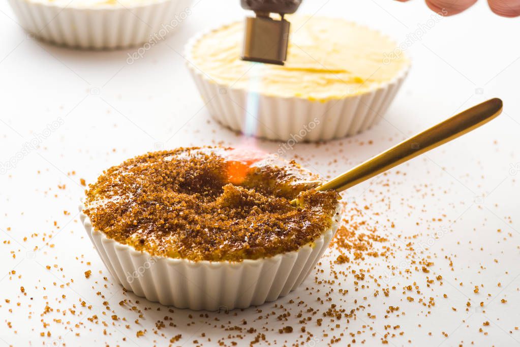 Caramelising sugar on top of creme brulee with flaming torch on a white background