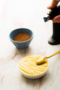 Creme catalana veya creme brulee satırlarının beyaz altın bir kaşık, bir kaynak makinesi ve kahverengi şeker kamışı ile karamelize hazır.