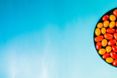 Mavi bir arka plan üzerinde mavi bir çanak üzerinde Kiraz renkli domates, üst görünümü, doğal ışık.