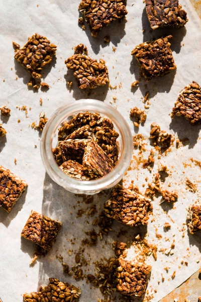 Healthy snack bar, typical   of russian diet, called kozinaki, made ith sunflower seeds and honey, on a wwhite food paper inside and outside a glass jar.