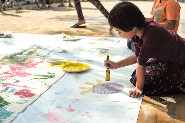 Portrait Asian little girl painting and drawing on the paper at outdoor art event for kids.