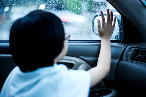 Portrait Asian girl sitting in car and looking out of window watching the rain. Girl feels bored of the traffic jam because of heavy rain