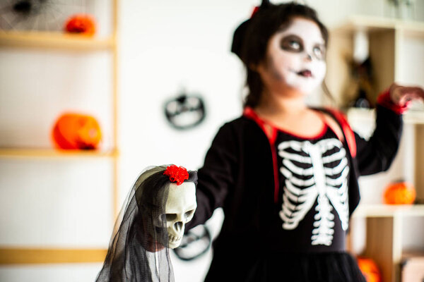 Blurred portrait Asian little girl in Halloween costume in background holding the skull