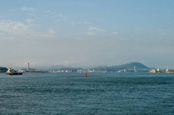 红色浮标漂浮在海上 背景是海景和地线 在背景下沿着城市景观和电缆桥沿着海洋旅行的船只 — 图库照片