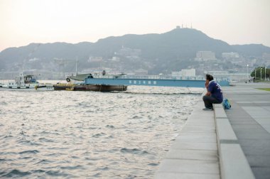 Nagasaki, Japonya: Ağustos 31, 2016 - portre Asya adam deniz oturan ve rüzgarlı gün okyanusun arıyorum. Sigara ve dışarı liman tüyler ürpertici bir adam.