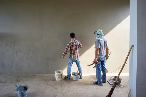 Back portrait of workers plastering the cement texture on the concrete wall with the sunlight at the house under construction