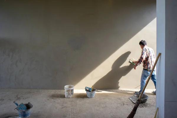 Back portrait of workers plastering the cement texture on the concrete wall with the sunlight at the house under construction