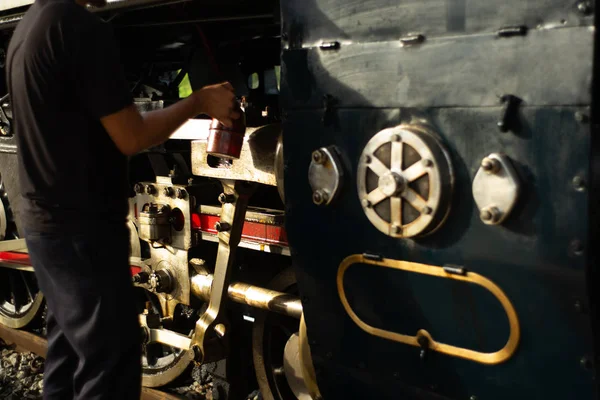 Closeup worker dropping the lubricant oil into the steel wheel of vintage train locomotive