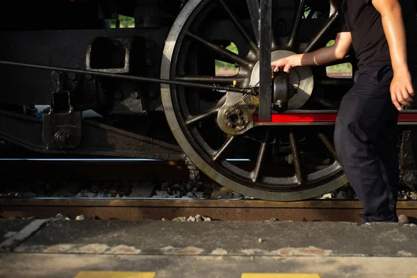 Closeup worker dropping the lubricant oil into the steel wheel of vintage train locomotive. Repair and maintenance concept
