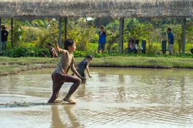 Portre Asya ıslak kız çamur gölet oynar sahiptir ve çiftlikte ördek grubu kovalar.