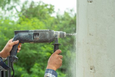 İşçinin yakın çekim elleri bir elektrik sondaj makinesi tutar ve çimento duvara matkaplar