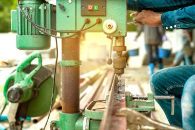 İşçinin ellerine yakınsama seçici odak gün batımı ışığı ile şantiyede açı çelik çubuğunda delik delme için elektrik sondaj makinesi kontrol