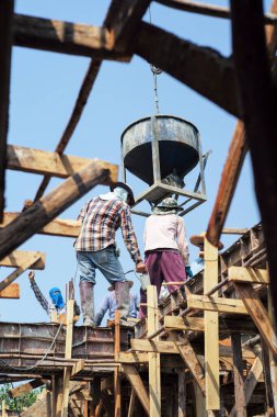 Yüksek melek manzaralı bir grup işçi vinçten sarkan büyük çelik kovadan karışık çimento döküyorlar..