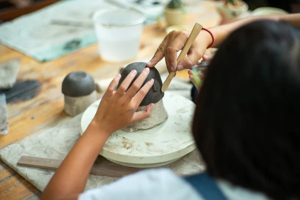 Closeup hand of teacher teachs the student in molding the clay with wooden tool.