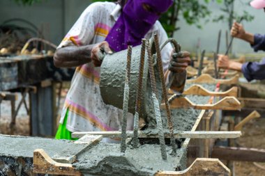 İnşaat alanındaki karışık çimento yapısına yakın takviye çelik. Arka planda bulanık işçiler var.