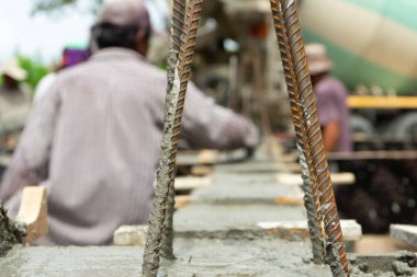 İnşaat alanındaki karışık çimento yapısına yakın takviye çelik. Arka planda bulanık işçiler var.
