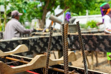 İnşaat alanındaki karışık çimento yapısına yakın takviye çelik. Arka planda bulanık işçiler var.