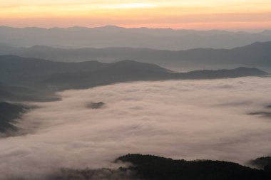 Dağ sıraları beyaz sisle kaplıydı ve sabah güneş doğuyordu.