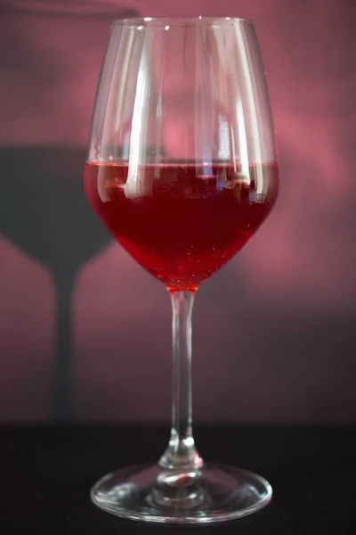 A glass of red wine, a background of red tint, the tank is illuminated with diffused light from the side, reflecting the shadow of glass on the left side