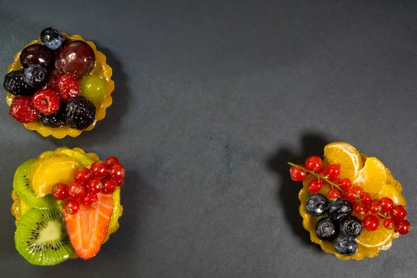 Taze biyo meyve, portakal, kivi, çilek, yaban mersini, kırmızı kuş üzümü, üzüm, ahududu, böğürtlen, yukarıda, fotoğraf ile üç kek siyah arka plan