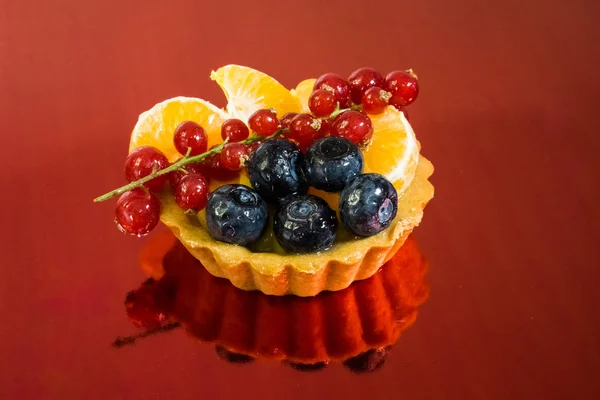 Cupcake with fresh bio fruit, orange, blueberry, red currant, side view photo, mirror red background