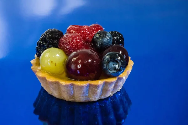 Pastel con bio frutas frescas, uvas, frambuesas, moras, vista lateral foto, espejo fondo azul — Foto de Stock