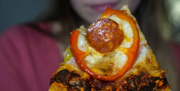 Una rebanada de pizza de pepperoni, la cara borrosa de una chica en el fondo, primer plano —  Fotos de Stock