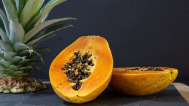 Papaya iki yarıya kesilir, stand ahşap çerçeveli bir taş tahta, Papay yakınında ananas bir kesik var, arka plan siyah