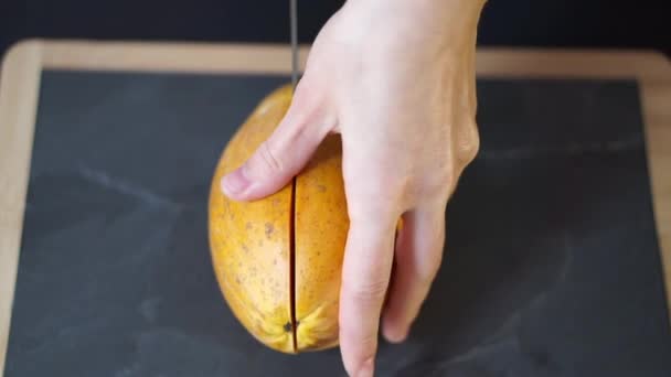 一个女人的双手拿一把刀 把黄色的木瓜切成两半 然后把两半拿来 拿去摄像机 然后用木架放在厨房的石板上 — 图库视频影像