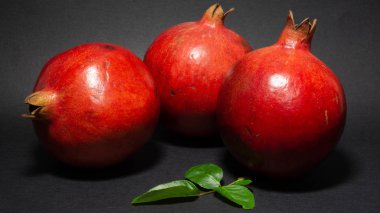 Parlak sulu nar meyve, siyah arka plan, fotoğraf üç meyve yakın, yeşil yaprakları, yakın çekim bulunmaktadır