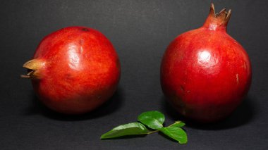 Parlak sulu nar meyve, siyah arka plan, fotoğraf iki meyve, yeşil yaprakları ile, yakın çekim