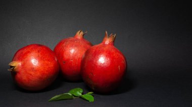 Parlak sulu nar meyve, siyah arka plan, fotoğraf üç meyve sol alt köşesinde bulunan, yeşil yaprakları ile, yakın çekim