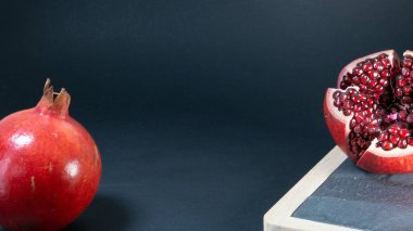 Nar meyve, sağda, meyve taş mutfak tahtası açık ve sol bir bütün nar, siyah arka plan.