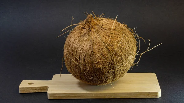Fruto exótico coco, fruta en la cáscara en una tabla de madera, fondo oscuro, enfoque selectivo, luz selectiva, primer plano —  Fotos de Stock