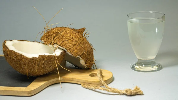 Fruta exótica de coco, dos mitades de cáscara de fruta en una cocina de piedra con mango de madera, junto a un vaso con agua de coco, con un fondo brillante, enfoque selectivo, primer plano —  Fotos de Stock