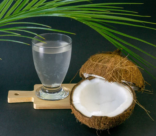 Frutos exóticos de coco, dos mitades de coco en la cáscara, fondo oscuro, un vaso de agua de coco en la cocina y pizarra, palmera, enfoque selectivo —  Fotos de Stock