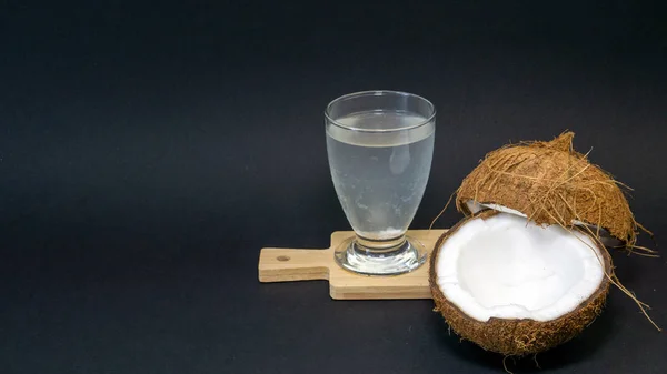Fruta exótica de coco, dos mitades de coco en la cáscara, fondo oscuro, un vaso de agua de coco en la cocina y pizarra, enfoque selectivo —  Fotos de Stock