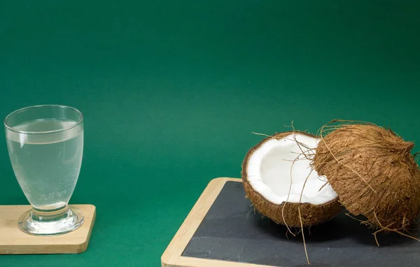 Fruta exótica de coco, dos mitades de coco en la cáscara, fondo verde, un vaso de agua de coco en la cocina y pizarra, enfoque selectivo —  Fotos de Stock