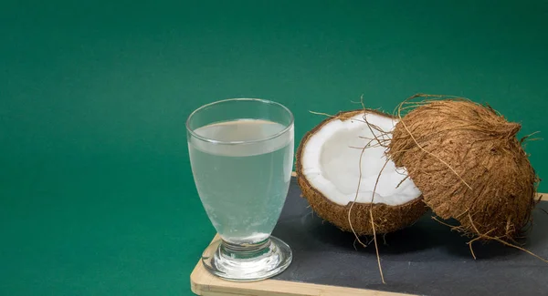 Fruta exótica de coco, dos mitades de fruta en la cáscara, fondo verde, un vaso de agua de coco en la cocina y pizarra, enfoque selectivo —  Fotos de Stock
